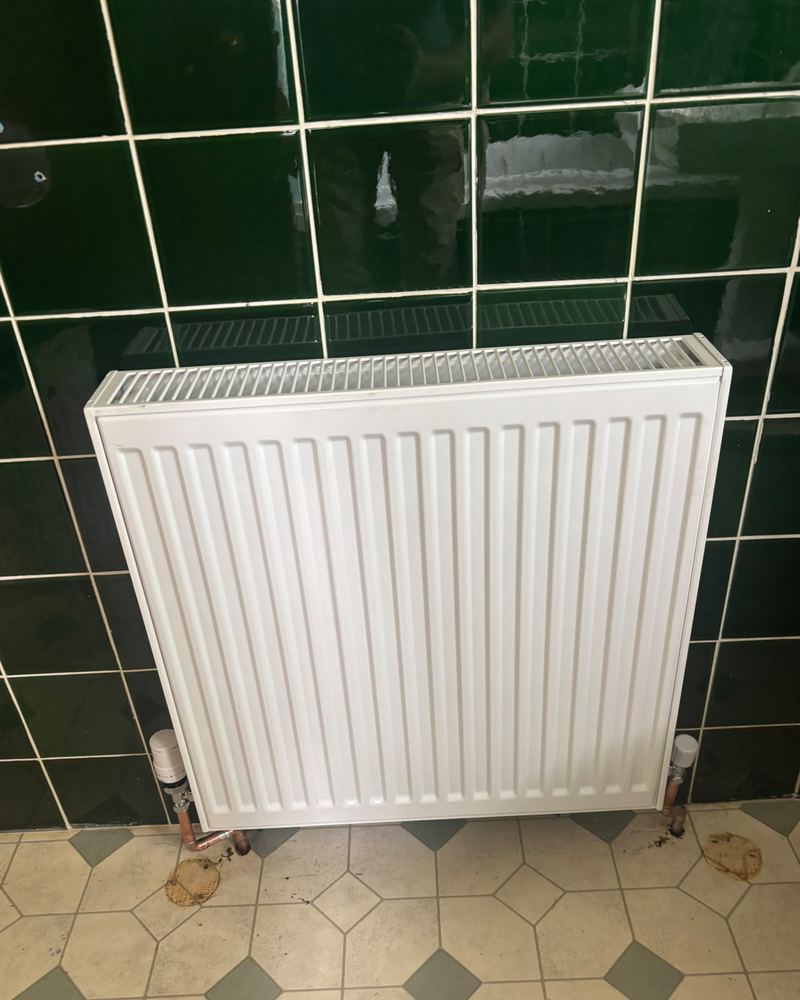 New radiator on a green tiled wall